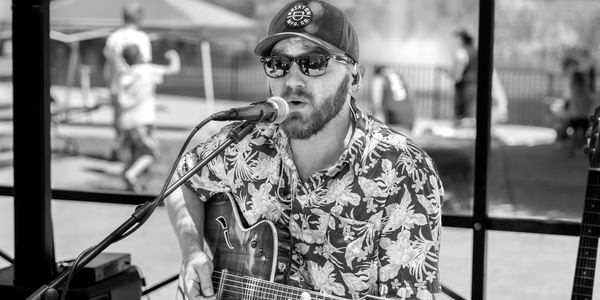 Alex Vincent singing and playing acoustic guitar at an outdoor gig